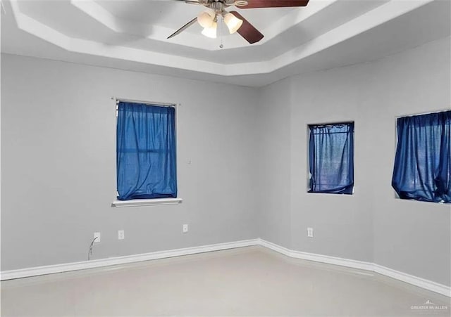 spare room with ceiling fan, baseboards, and a tray ceiling