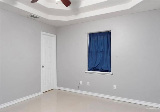 empty room with a tray ceiling, visible vents, baseboards, and ceiling fan