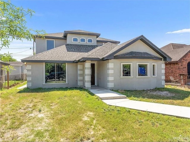 view of front facade featuring stucco siding, a shingled roof, a front yard, and fence