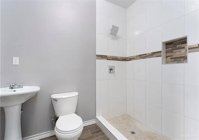 full bathroom with wood finished floors, baseboards, tiled shower, a sink, and toilet