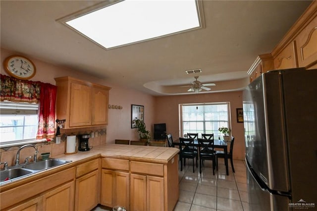 kitchen with sink, stainless steel fridge, light tile patterned floors, tile counters, and kitchen peninsula