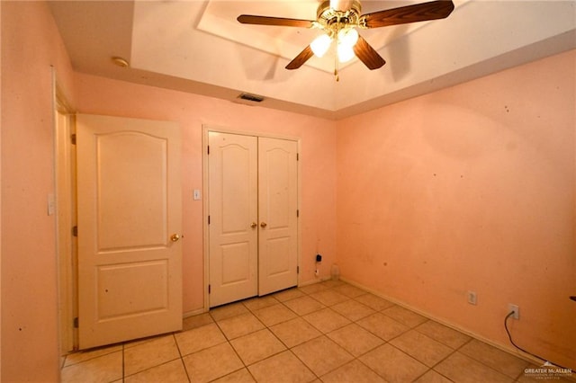 unfurnished bedroom featuring light tile patterned floors, a closet, a raised ceiling, and ceiling fan