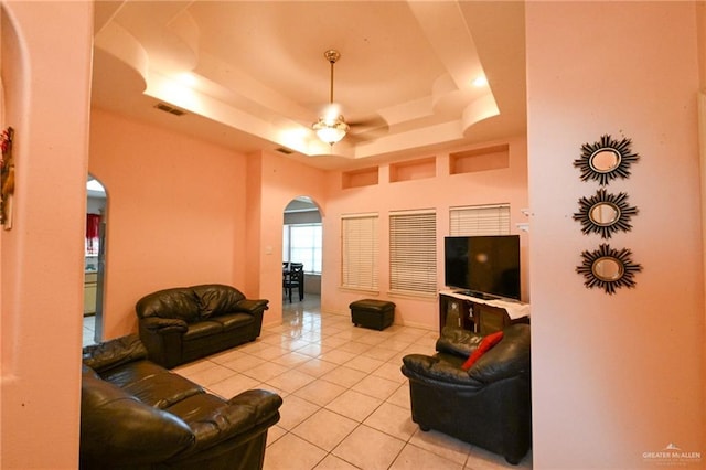 living room featuring a raised ceiling, ceiling fan, and light tile patterned flooring