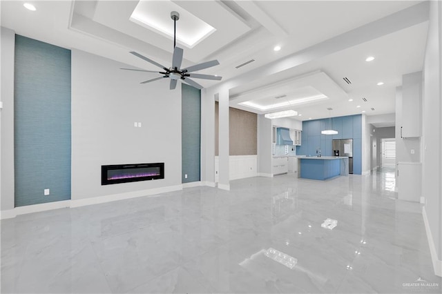 unfurnished living room with ceiling fan and a tray ceiling