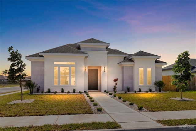 view of front facade featuring stucco siding, a front lawn, fence, and a shingled roof