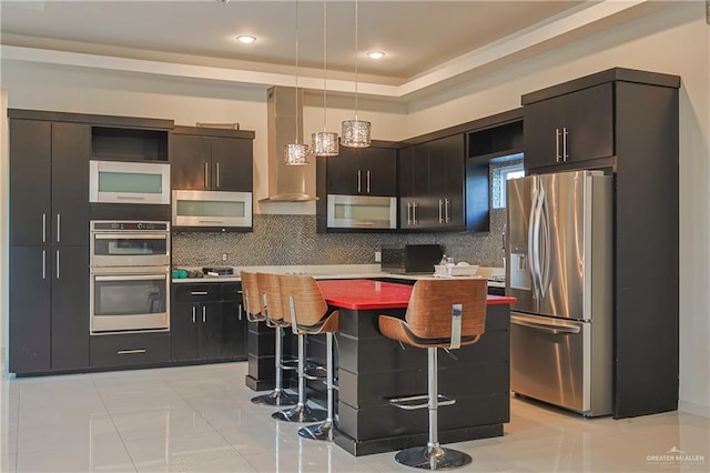 kitchen with wall chimney exhaust hood, appliances with stainless steel finishes, a kitchen island, and a breakfast bar area