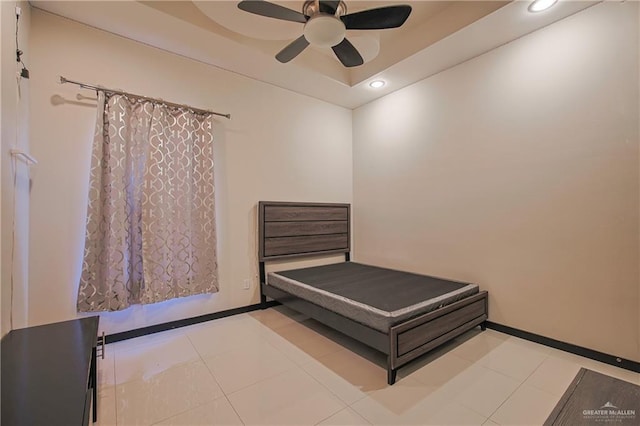 bedroom with a raised ceiling, light tile patterned flooring, and ceiling fan