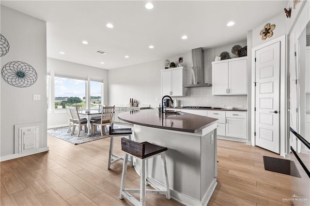 kitchen with sink, a breakfast bar area, a kitchen island with sink, white cabinets, and wall chimney exhaust hood