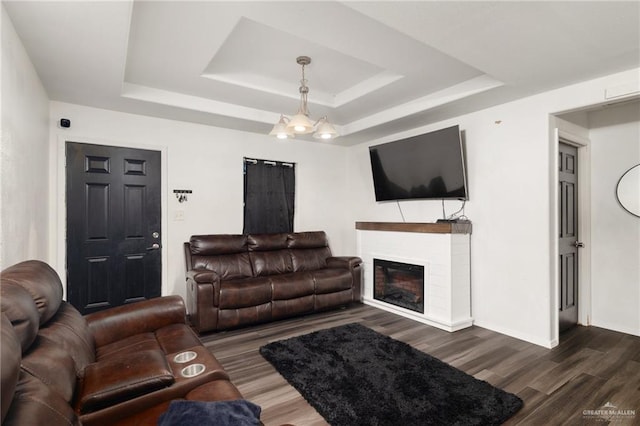 living room featuring a tray ceiling, dark wood-type flooring, and an inviting chandelier