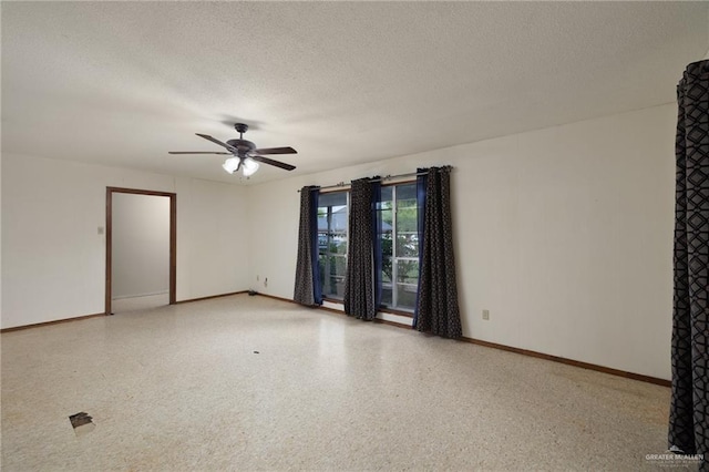 empty room with a textured ceiling, speckled floor, a ceiling fan, and baseboards