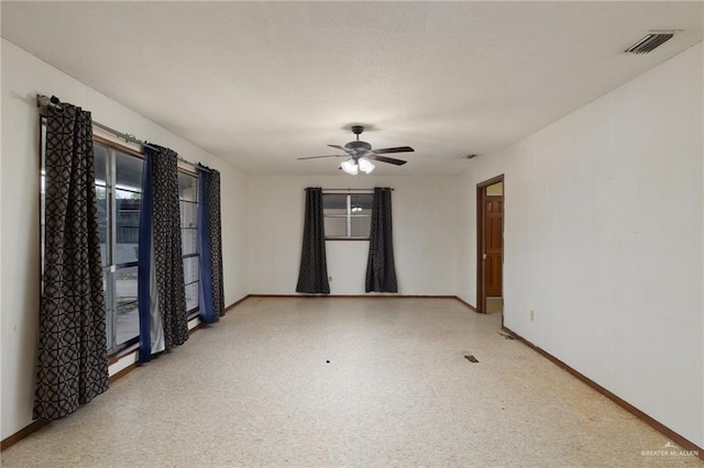 empty room featuring a ceiling fan, visible vents, a wealth of natural light, and baseboards