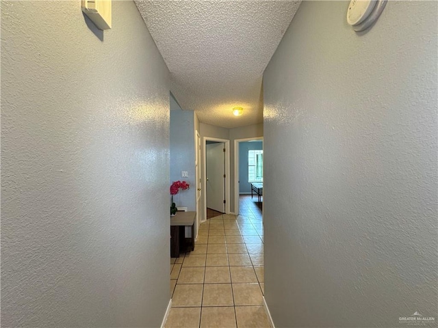 hall with a textured wall, a textured ceiling, and light tile patterned floors