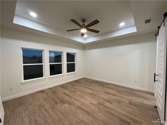 1513 Helen Dr, Weslaco, TX 78596 - unfurnished room featuring a barn door, a tray ceiling, a ceiling fan, wood finished floors, and baseboards