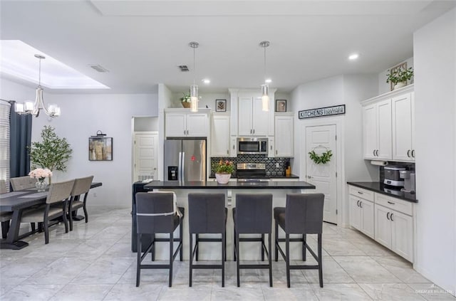 kitchen with a center island with sink, stainless steel appliances, dark countertops, hanging light fixtures, and white cabinets