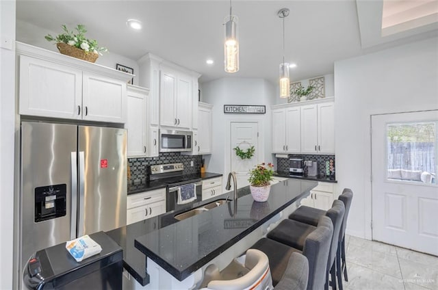 kitchen with a kitchen island with sink, stainless steel appliances, white cabinetry, backsplash, and pendant lighting