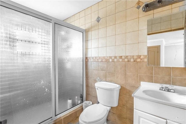 bathroom featuring toilet, tile walls, a shower with shower door, and vanity