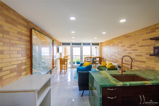 kitchen featuring dark brown cabinetry, sink, and brick wall