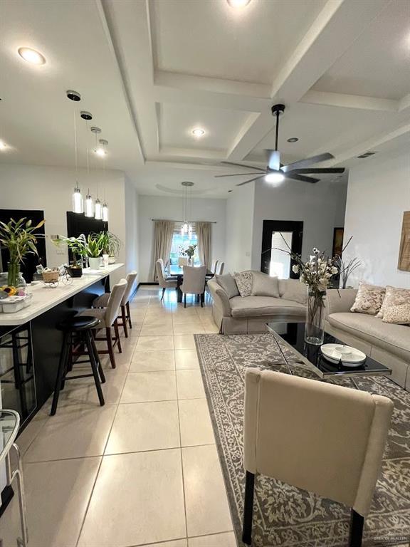 living room with beam ceiling, coffered ceiling, a ceiling fan, and light tile patterned flooring