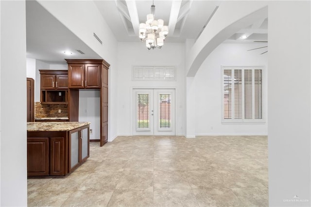 interior space featuring french doors, backsplash, light stone counters, ceiling fan with notable chandelier, and dark brown cabinetry