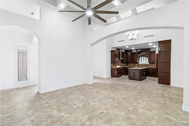 unfurnished living room with beamed ceiling, a high ceiling, ceiling fan with notable chandelier, and light tile patterned floors