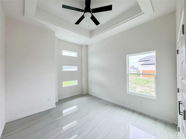 unfurnished room with a tray ceiling, ceiling fan, and baseboards