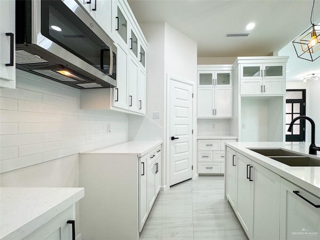 kitchen featuring visible vents, decorative backsplash, glass insert cabinets, stainless steel microwave, and a sink
