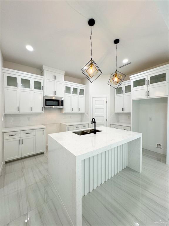 kitchen with an island with sink, a sink, stainless steel microwave, and white cabinets