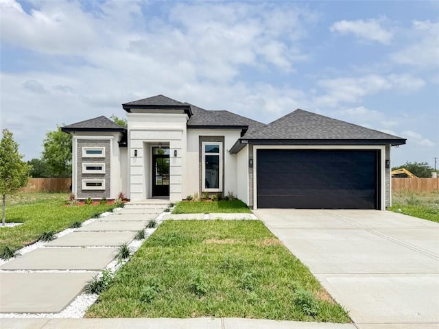 prairie-style house featuring driveway, a front yard, fence, an attached garage, and a shingled roof