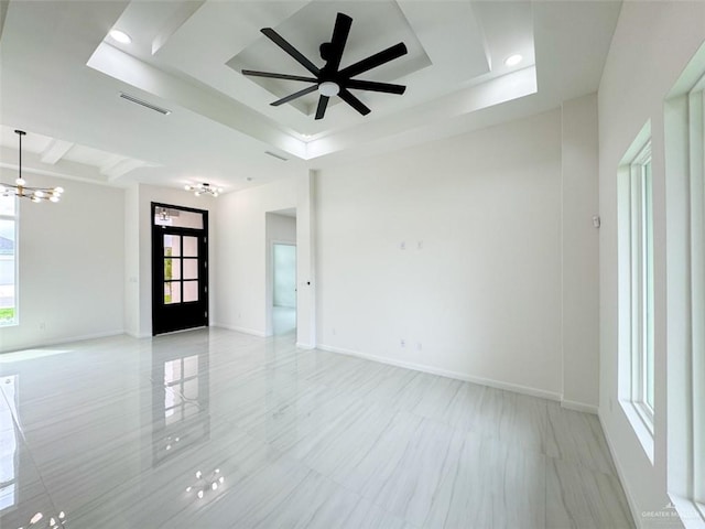 spare room with a tray ceiling, visible vents, baseboards, and ceiling fan with notable chandelier