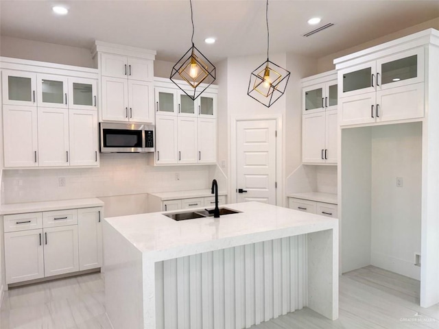 kitchen with a sink, stainless steel microwave, backsplash, visible vents, and a center island with sink