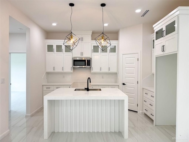 kitchen featuring visible vents, a center island with sink, stainless steel microwave, tasteful backsplash, and a sink