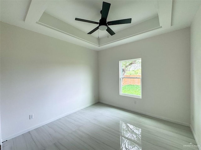 spare room with a ceiling fan, baseboards, a raised ceiling, and light wood-style floors