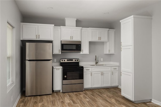 kitchen with light wood-style flooring, appliances with stainless steel finishes, light countertops, white cabinetry, and a sink