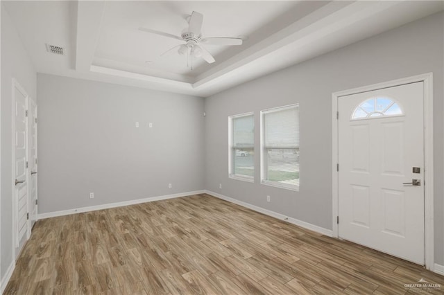 entrance foyer with a raised ceiling, visible vents, light wood-style flooring, and baseboards