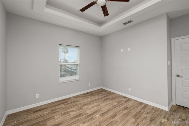 spare room with a tray ceiling, visible vents, a ceiling fan, light wood-type flooring, and baseboards