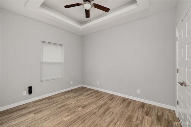 empty room with a raised ceiling, light wood-style flooring, and baseboards