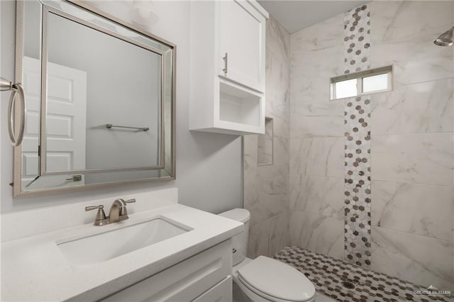 bathroom with toilet, a tile shower, and vanity