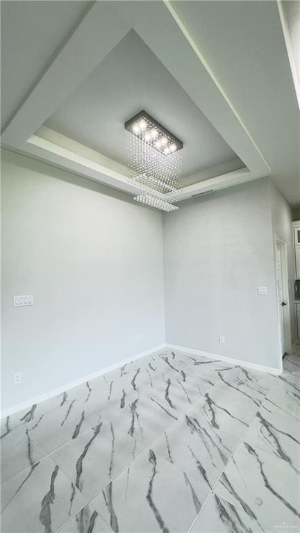 empty room featuring baseboards, a raised ceiling, and marble finish floor