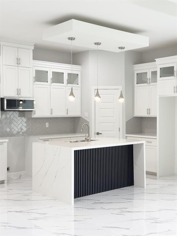 kitchen with a sink, hanging light fixtures, glass insert cabinets, white cabinetry, and marble finish floor