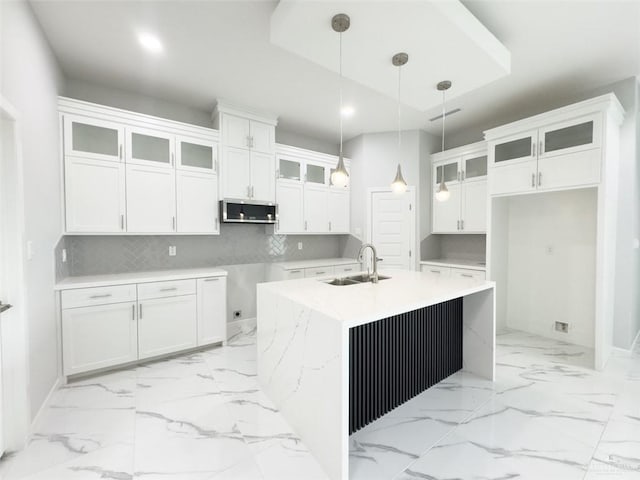 kitchen featuring a center island with sink, a sink, marble finish floor, stainless steel microwave, and tasteful backsplash