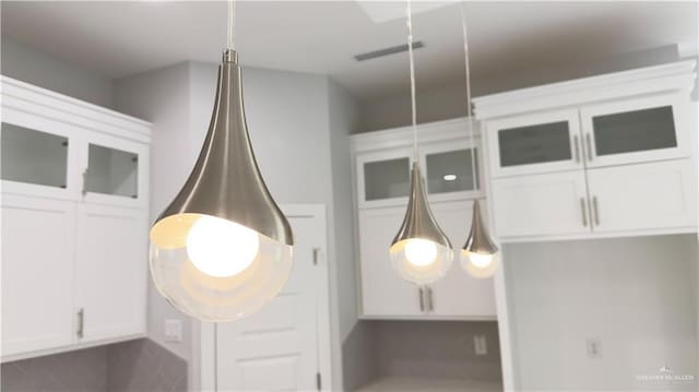 interior details with visible vents, white cabinetry, and glass insert cabinets