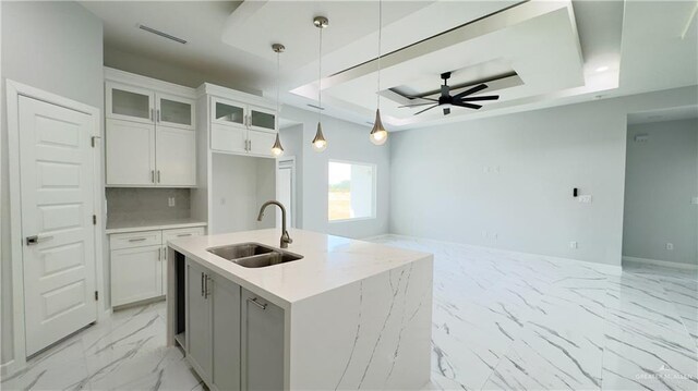 kitchen with a ceiling fan, a sink, marble finish floor, a raised ceiling, and open floor plan