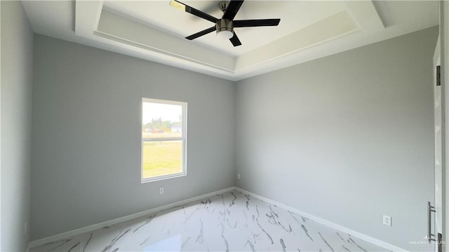 spare room featuring a ceiling fan, a tray ceiling, baseboards, and marble finish floor