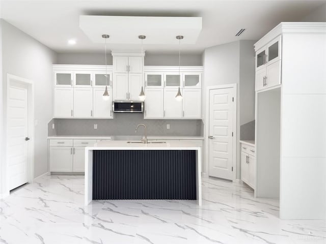 kitchen with a kitchen island with sink, a sink, stainless steel microwave, marble finish floor, and backsplash