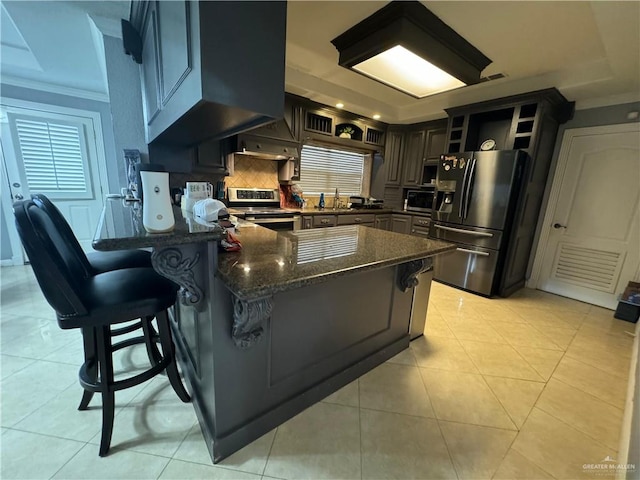 kitchen featuring dark stone countertops, a breakfast bar, light tile patterned floors, and stainless steel appliances