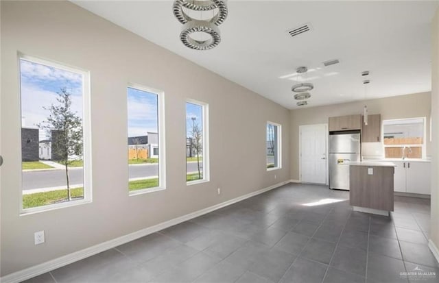 interior space featuring a healthy amount of sunlight, decorative light fixtures, stainless steel refrigerator, and a kitchen island