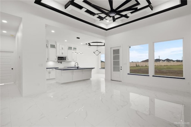 kitchen with white cabinetry, sink, a towering ceiling, decorative light fixtures, and a kitchen island with sink