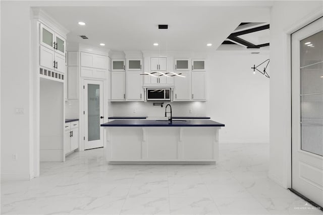 kitchen with beamed ceiling, decorative backsplash, white cabinetry, and an island with sink