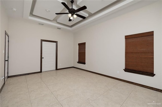 empty room featuring light tile patterned floors, visible vents, baseboards, ceiling fan, and a tray ceiling