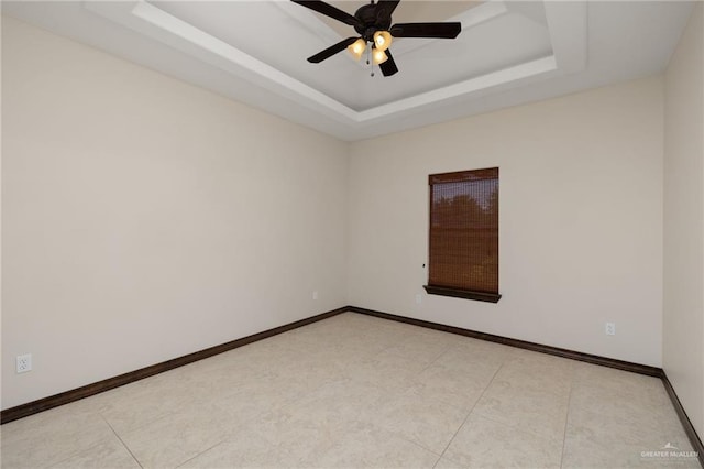 spare room featuring a tray ceiling, ceiling fan, and baseboards